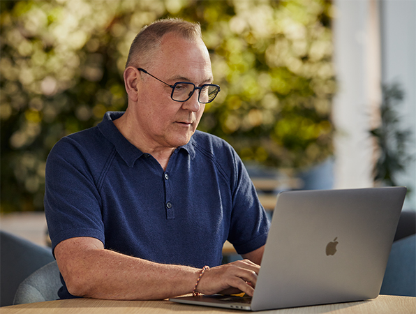 Pracownik działu Software and Services w ośrodku Apple na tle zieleni, który pracuje na dworze na MacBooku.