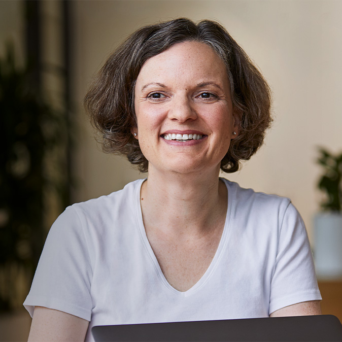 Uśmiechnięta Ruth siedząca w pomieszczeniu z roślinami w tle.