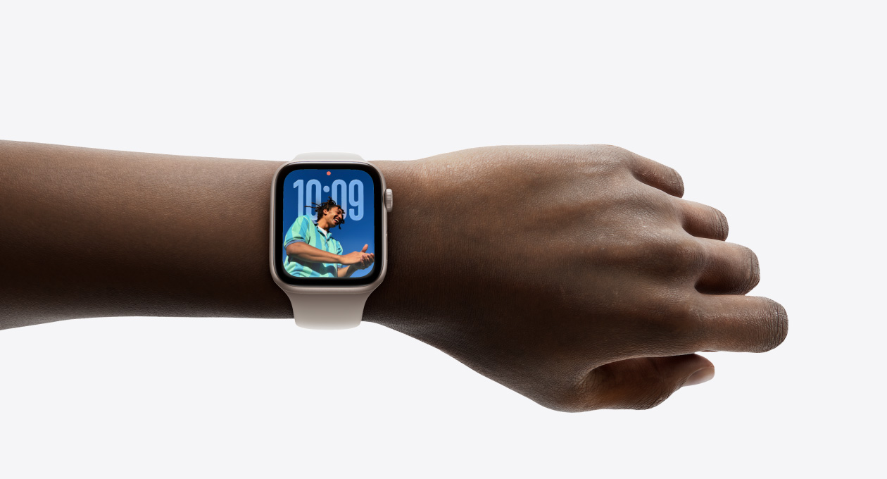 特寫畫面顯示手腕上戴著配上橡膠錶帶的星光色 Apple Watch，展示全新 Liquid Glass 設計的時鐘 app