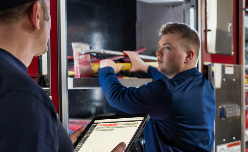 Deux membres de l’équipe inspectent les outils et équipements d’un camion de pompiers ; l’un tient un iPad à la main pendant que l’autre mène l’inspection 