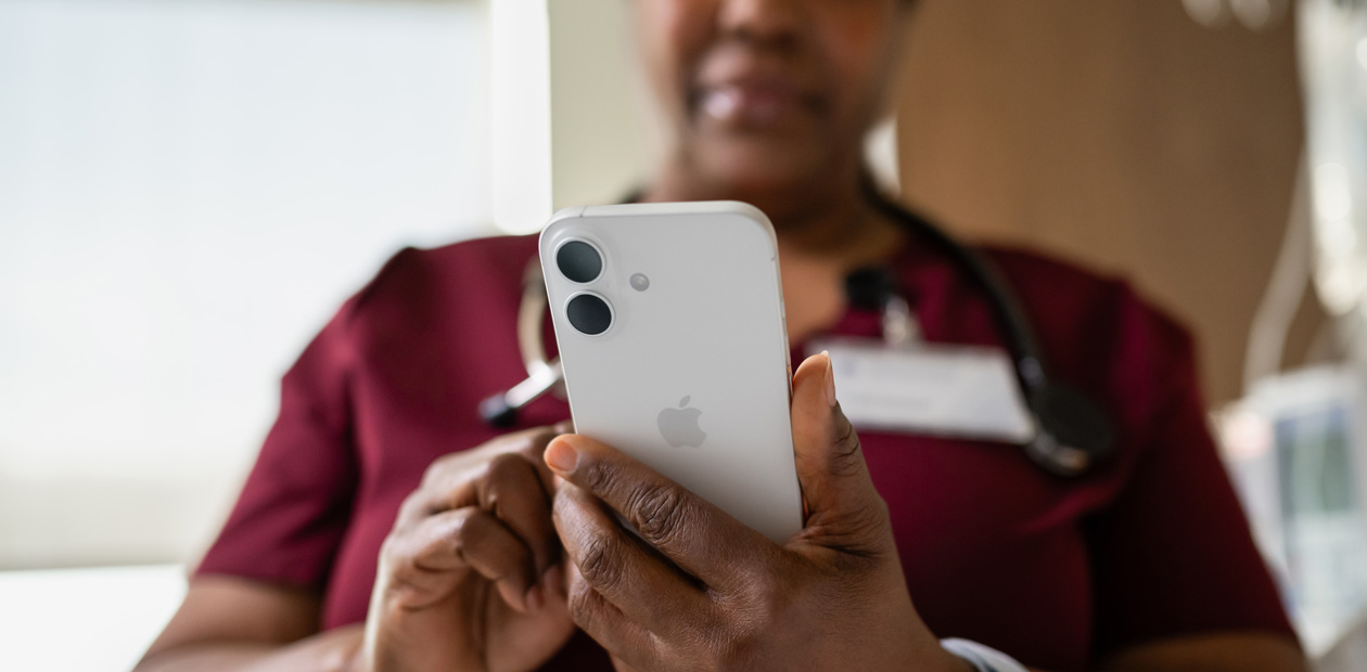 Uma enfermeira com uniforme vermelho consulta seu iPhone durante o atendimento.
