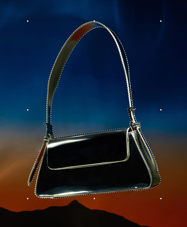 Eine schwarze Handtasche, die mit gestrichelten Linien eingefasst ist, Auswahltool, Bildbearbeitung, Hintergrund mit Sonnenuntergang und der Silhouetten von Bergen